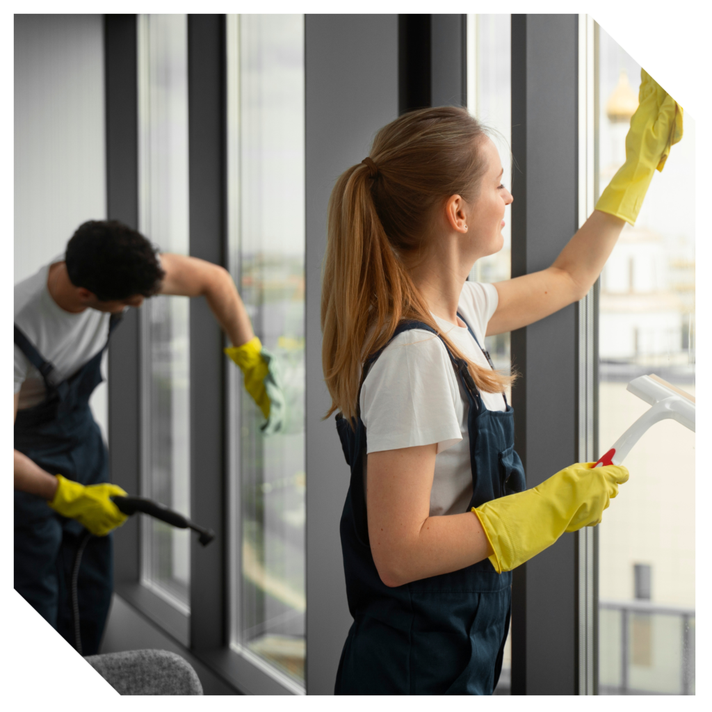 Two workers in yellow gloves meticulously clean the interior windows; one wipes with a cloth while the other skillfully maneuvers a squeegee, ensuring a pristine finish.